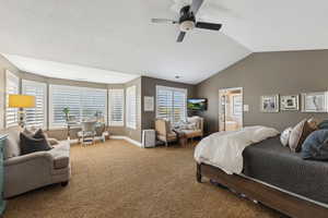 Carpeted bedroom featuring vaulted ceiling, a ceiling fan, and ensuite bath