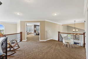 Hallway featuring a chandelier, an upstairs landing, crown molding, and carpet floors