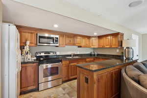 Kitchen with stainless steel appliances, wood finish cabinetry, a peninsula, recessed lighting, and dark stone counters