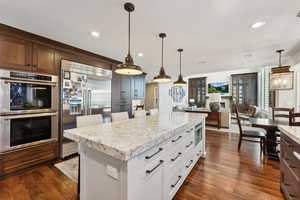 Kitchen featuring built in appliances, light stone countertops, dark wood-style floors, a kitchen island, and a breakfast bar area