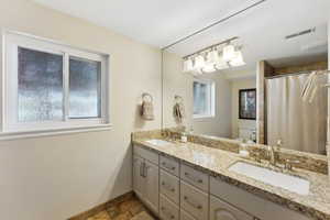 Full bathroom with double vanity, a shower with curtain, stone tile flooring, and plenty of natural light
