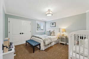 Bedroom featuring a closet, dark colored carpet, ornamental molding, and a textured ceiling