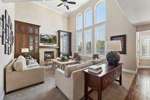 Living area with a high ceiling, a tiled fireplace, a ceiling fan, ornamental molding, and dark wood-style floors