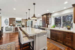 Two tone kitchen featuring two tone color scheme, a kitchen breakfast bar, light stone counters, a center island, and dark wood-type flooring