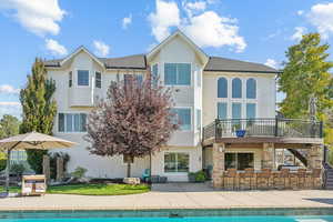 Rear view of house with stucco siding, an outdoor pool, a patio area, exterior bar, and roof with shingles