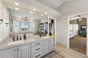 Bathroom featuring vaulted ceiling, light carpet, ensuite bathroom, double vanity, and recessed lighting