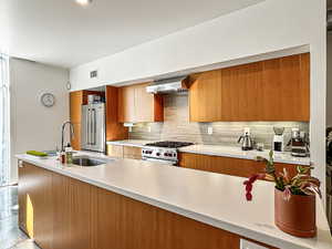 Kitchen featuring modern cabinets, high end appliances, wood finish cabinets, tasteful backsplash, and light stone counters