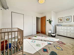 Bedroom with a closet, a crib, and light colored carpet