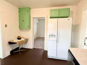 Kitchen with white refrigerator with ice dispenser, green cabinetry, stainless steel dishwasher, and tile countertops