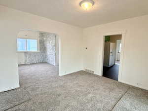 Carpeted empty room with a textured ceiling and arched walkways