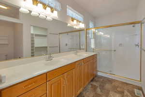 Bathroom with double vanity, stone finish floors, a shower stall, and a walk in closet
