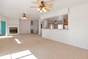 Unfurnished living room featuring light colored carpet, a glass covered fireplace, and a ceiling fan
