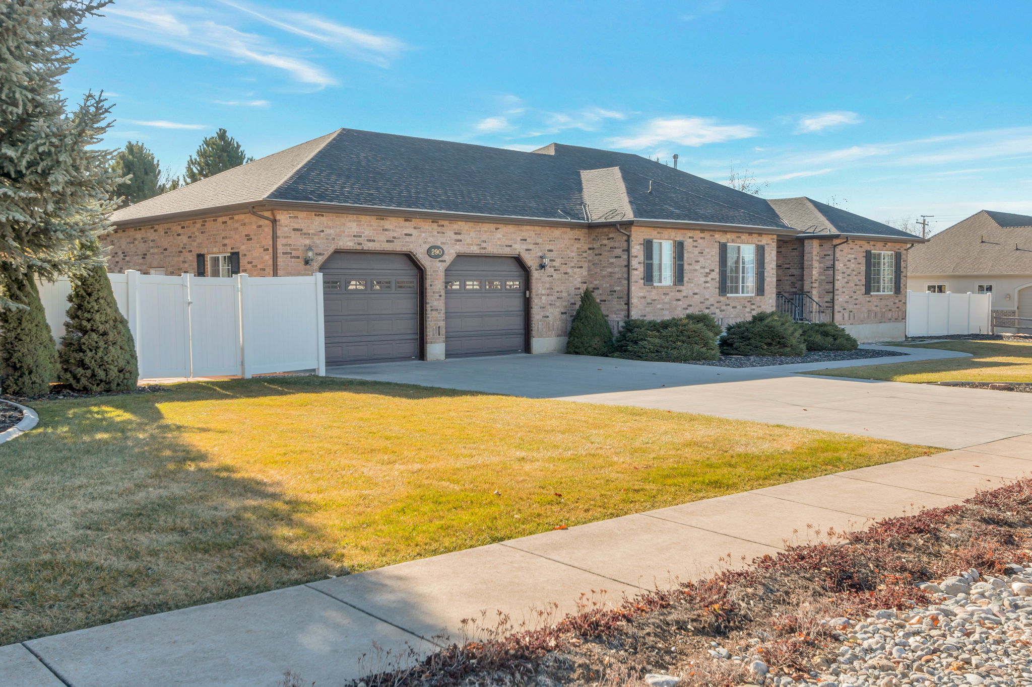 View of side of home with a shingled roof, an attached garage, driveway, brick siding, and a gate