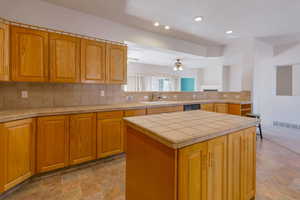 Kitchen featuring tile counters, a center island, ceiling fan, backsplash, and recessed lighting