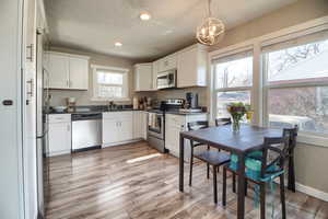Kitchen with stainless steel appliances, white cabinetry, dark countertops, light wood-type flooring, and suspended lighting