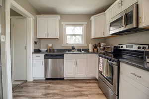 Kitchen featuring stainless steel appliances, white cabinetry, light wood-style flooring, and dark stone countertops