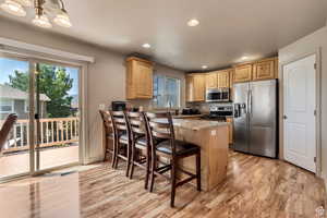 Kitchen with stainless steel appliances, light wood-style floors, a peninsula, a breakfast bar, and light wood finish cabinets