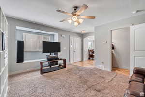 Living area with arched walkways, light carpet, and ceiling fan