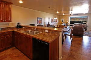 Kitchen featuring dark countertops, a peninsula, open floor plan, dishwasher, and a ceiling fan