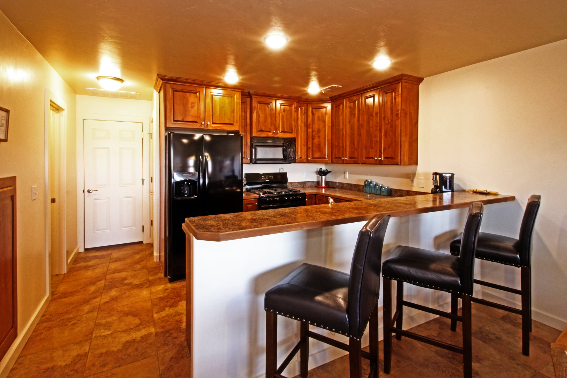 Kitchen with dark countertops, black appliances, a kitchen breakfast bar, a peninsula, and wood finish cabinetry