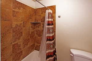 Bathroom featuring toilet and shower / bathtub combination with curtain