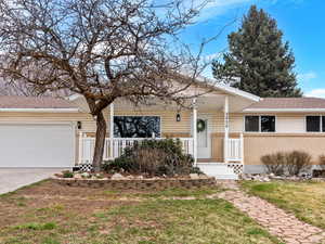 Ranch-style home featuring an attached garage, brick siding, a porch, concrete driveway, and a front yard