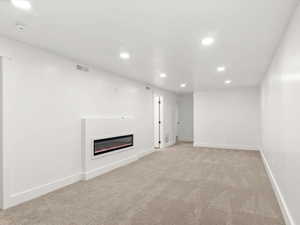 Basement featuring a glass covered fireplace, light carpet, and recessed lighting