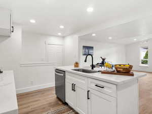 Kitchen with light wood-type flooring, white cabinetry, light stone counters, a kitchen island with sink, and dishwasher