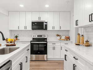 Kitchen featuring stainless steel appliances, light stone counters, white cabinets, and recessed lighting