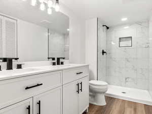 Full bathroom featuring double vanity, a shower stall, and dark wood-style floors