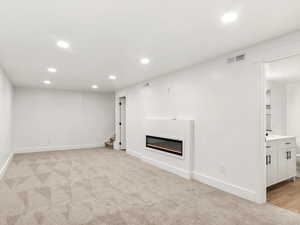 Finished below grade area with recessed lighting, light carpet, and a glass covered fireplace