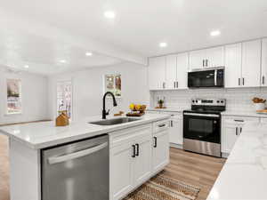 Kitchen with stainless steel appliances, white cabinets, light stone countertops, recessed lighting, and a kitchen island with sink