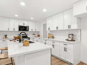 Kitchen with white cabinetry, a center island with sink, light wood finished floors, light stone counters, and recessed lighting