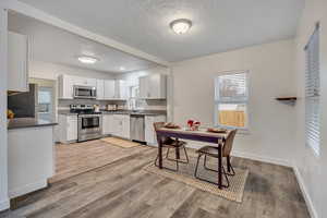 Kitchen featuring stainless steel appliances, white cabinetry, light wood-style floors, a textured ceiling, and tasteful backsplash