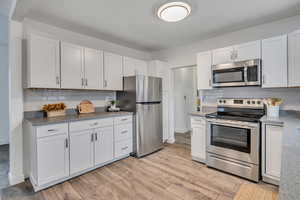 Kitchen featuring stainless steel appliances, white cabinetry, light wood-style flooring, and decorative backsplash
