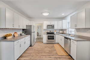 Kitchen with stainless steel appliances, white cabinetry, decorative backsplash, and recessed lighting
