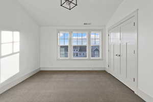 Unfurnished bedroom with lofted ceiling and dark colored carpet