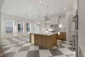 Kitchen with dark floors, a kitchen island with sink, hanging lights, two tone cabinetry, and glass fronted cabinets