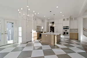 Dual tone kitchen featuring a chandelier, decorative backsplash, two tone cabinets, glass insert cabinets, and dark floors