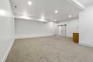 Empty room with a barn door, light colored carpet, and recessed lighting