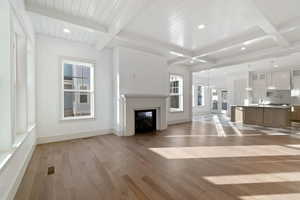 Unfurnished living room with light wood-style flooring, a glass covered fireplace, hanging lights, and a wood ceiling with exposed beams