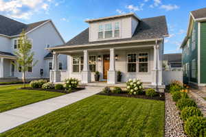 Craftsman-style home featuring a covered front porch with square columns, white siding, a dark shingle roof, and a wood-finish front door