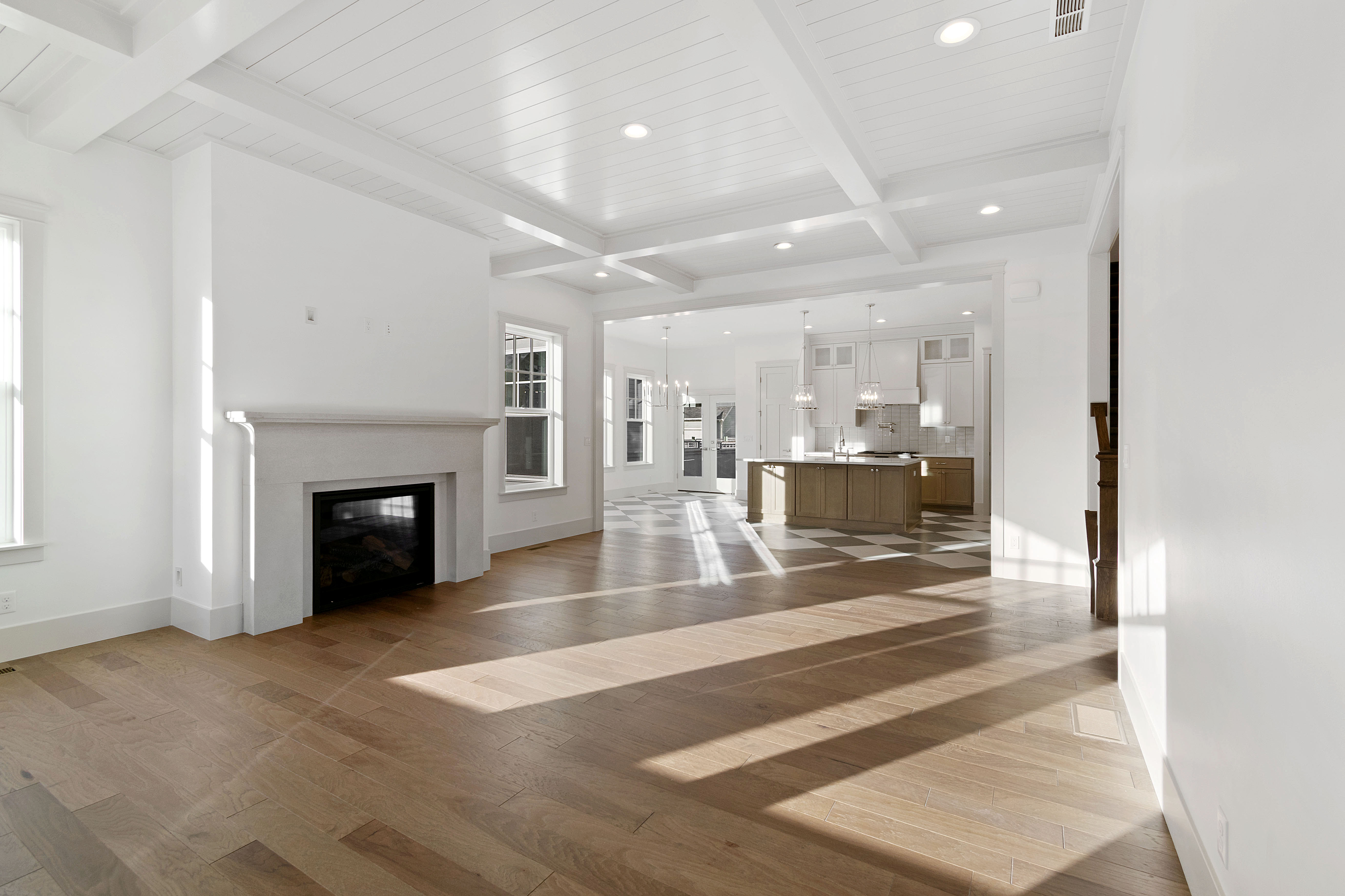Unfurnished living room featuring beam ceiling, a glass covered fireplace, light wood finished floors, and hanging lights
