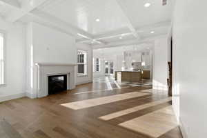 Unfurnished living room featuring beam ceiling, a glass covered fireplace, light wood finished floors, and hanging lights