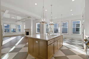 Kitchen featuring light floors, a kitchen island with sink, open floor plan, a fireplace, and beamed ceiling
