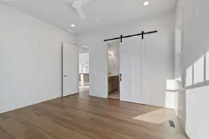 Unfurnished bedroom featuring a barn door, light wood finished floors, a ceiling fan, connected bathroom, and recessed lighting