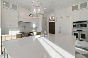 Kitchen with glass fronted cabinets, white cabinets, stainless steel appliances, and tasteful backsplash
