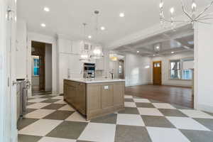 Two tone kitchen featuring a chandelier, open floor plan, an island with sink, dual tone cabinetry, and stainless steel appliances