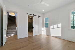 Unfurnished bedroom featuring a barn door, light wood-style floors, a ceiling fan, ensuite bathroom, and recessed lighting