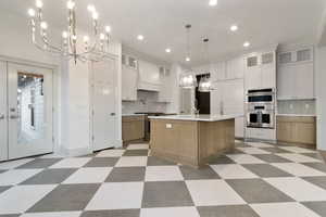 Two tone kitchen with a chandelier, two tone cabinets, glass insert cabinets, and light floors